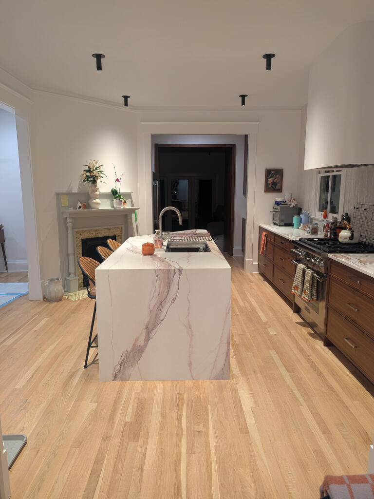 A freshly cleaned kitchen with a marble island, warm wood floors, and soft lighting. A small pumpkin and styled decor add seasonal warmth. The space feels personal, polished, and professionally refreshed.